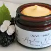 Organic anti aging face cream in glass jar with lid off, showcasing its smooth texture next to fresh blackberries and flowers.
