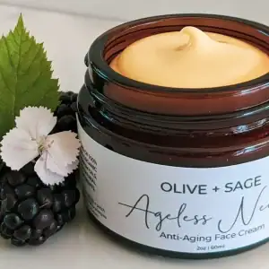 Organic anti aging face cream in glass jar with lid off, showcasing its smooth texture next to fresh blackberries and flowers.