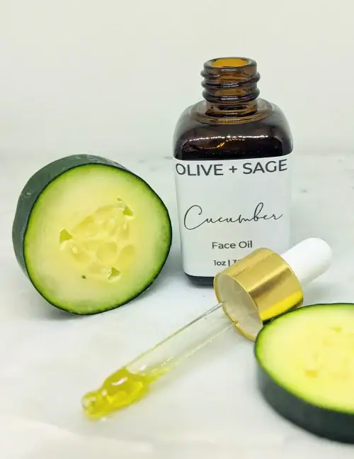 Organic Cucumber Face Oil in glass dropper bottle with dropper out and sliced cucumbers surrounding the bottle.
