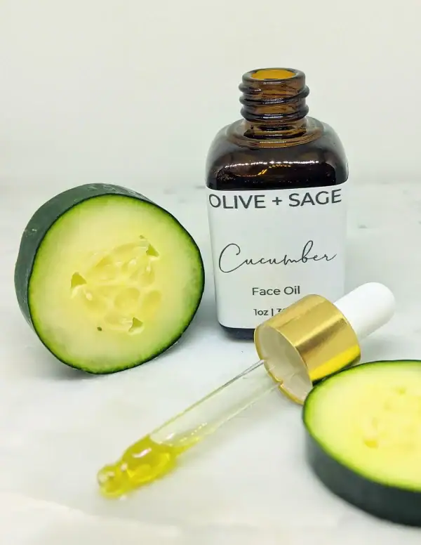 Organic Cucumber Face Oil in glass dropper bottle with dropper out and sliced cucumbers surrounding the bottle.