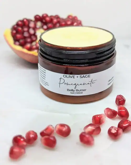 Organic Belly Balm in jar with lid off surrounded by pomegranates, perfect for preventing stretch marks during pregnancy.