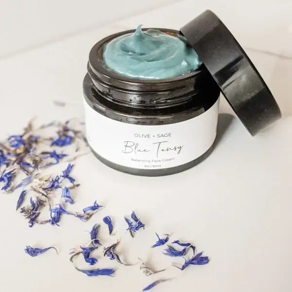 Blue tansy moisturizer jar and petals—natural hydration for sensitive, redness-prone skin.