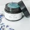 Jar of Organic Blue Tansy Moisturizer surrounded by blue tansy flowers, ideal for calming sensitive skin.