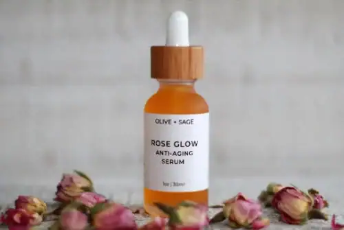 Close-up of Rose Glow Anti-Aging Serum in glass dropper bottle with dried roses around it