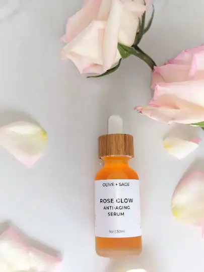 Rose Glow Anti-Aging Serum dropper bottle lying down with pink and white roses around it