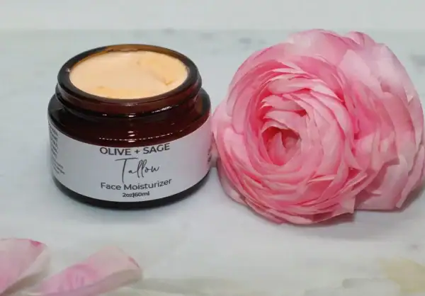 Smooth texture of whipped tallow cream in a glass jar with pink rose beside it.