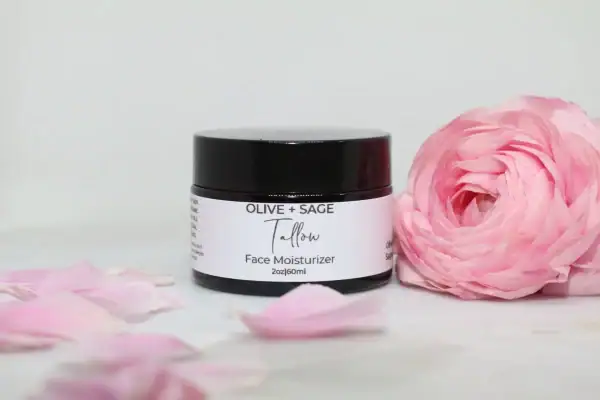 Whipped tallow cream in a glass jar with lid on, pink rose beside it, showcasing natural skincare.