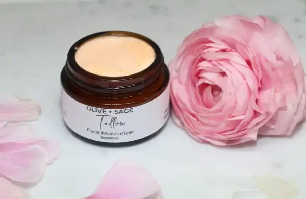 Close-up of whipped tallow cream texture in a glass jar with pink rose accent.