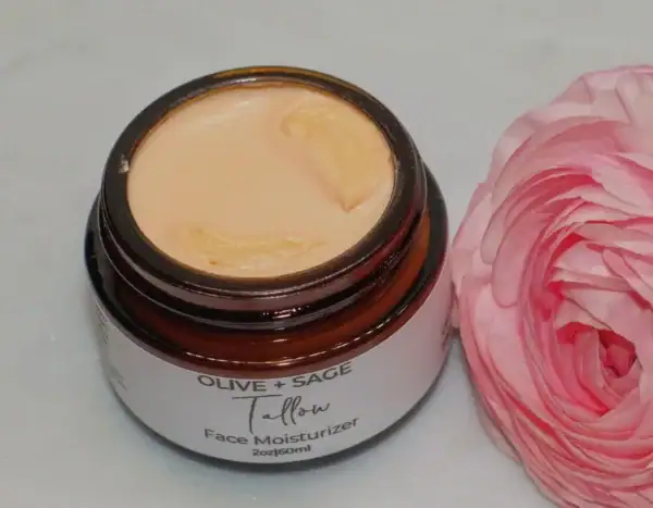 Whipped tallow cream in a glass jar showing texture and color with pink rose beside it.