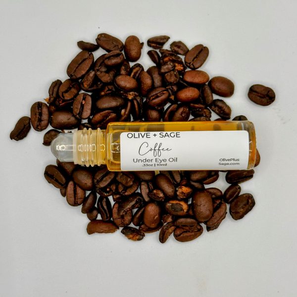 Organic Coffee Under Eye Oil with the top off from a side view on coffee beans