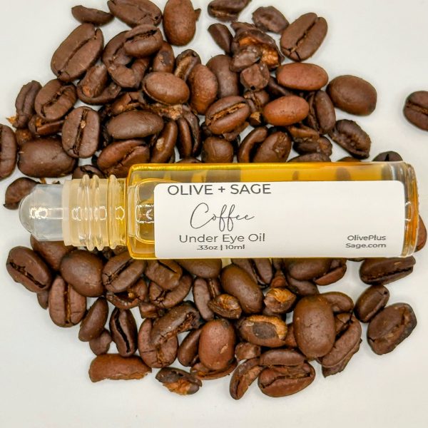 Organic Coffee Under Eye Oil with the top off, placed on coffee beans