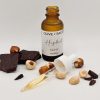 Straight-on lightbox photo of organic hazelnut face oil with dropper, surrounded by cocoa and hazelnuts