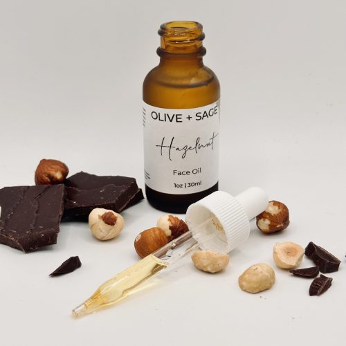Straight-on lightbox photo of organic hazelnut face oil with dropper, surrounded by cocoa and hazelnuts