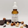 Glass bottle of organic hazelnut face oil with top on, styled with chocolate and raw hazelnuts