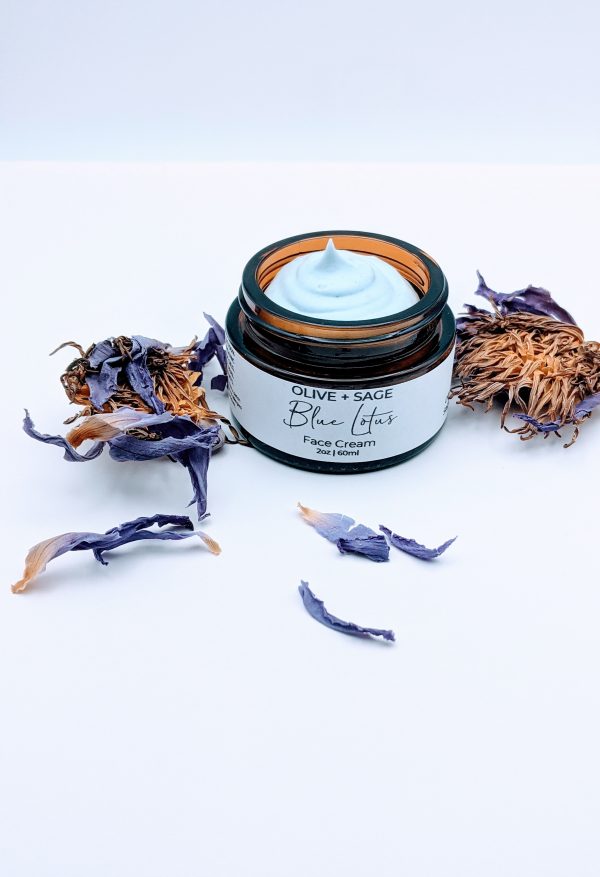 ngled view of Blue Lotus Face Cream jar with visible creamy texture and lotus leaves. Made with squalane, cupuaçu butter, and calming oils.