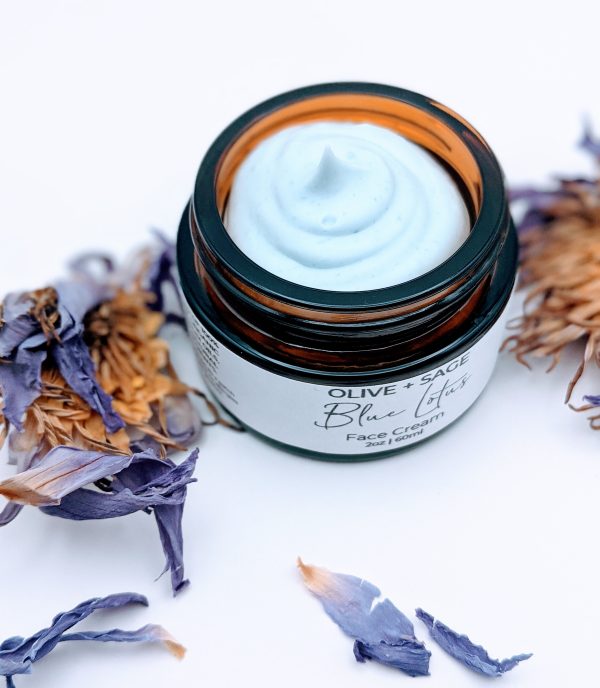 Closeup of Blue Lotus Face Cream 1 oz glass jar surrounded by lotus petals. Natural face cream for redness-prone, sensitive skin.