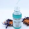 Blue Lotus Face Oil dropper dripping golden facial oil with blue lotus flowers in background, soothing skincare for redness-prone skin
