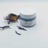 Closed jar of Blue Lotus Face Scrub with a fresh blue lotus flower beside it