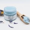 Wooden scoop of Blue Lotus Face Scrub resting in an open jar