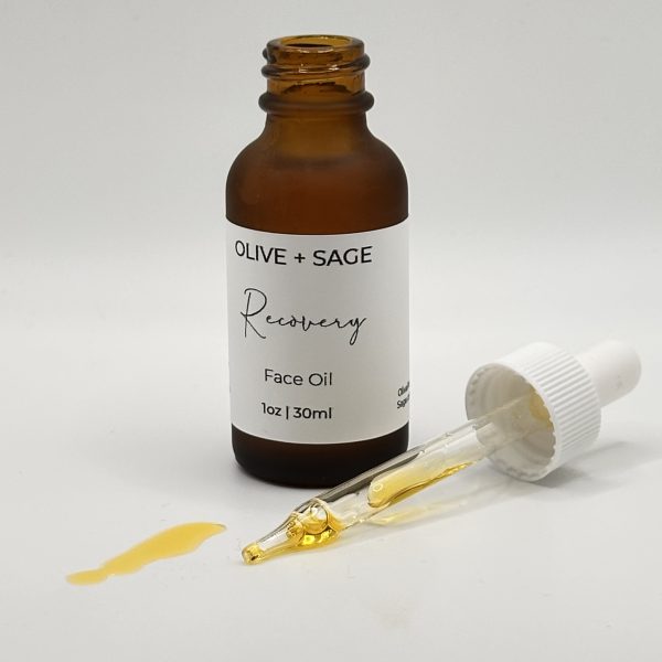Recovery Face Oil in amber glass bottle with dropper and golden botanical oil spill.